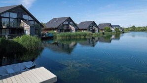 A row of modern houses with large windows and a calm water body in the foreground.