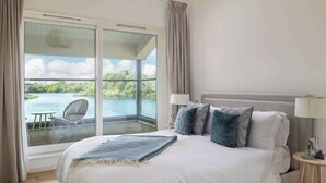 A bedroom with a large bed, a nightstand, and a view of a lake through a sliding glass door.