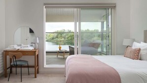Une chambre à coucher comprenant un lit, un bureau avec une chaise, un miroir et un balcon donnant sur un espace verdoyant.