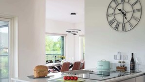 Une cuisine moderne dotée d’une grande horloge murale, d’un îlot central avec un plan de travail en verre et d’un coin repas offrant une vue agréable.