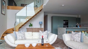 A modern living room with a white sofa, a wooden coffee table, and a staircase with glass railings. - Egret Lodge (South Cerney)