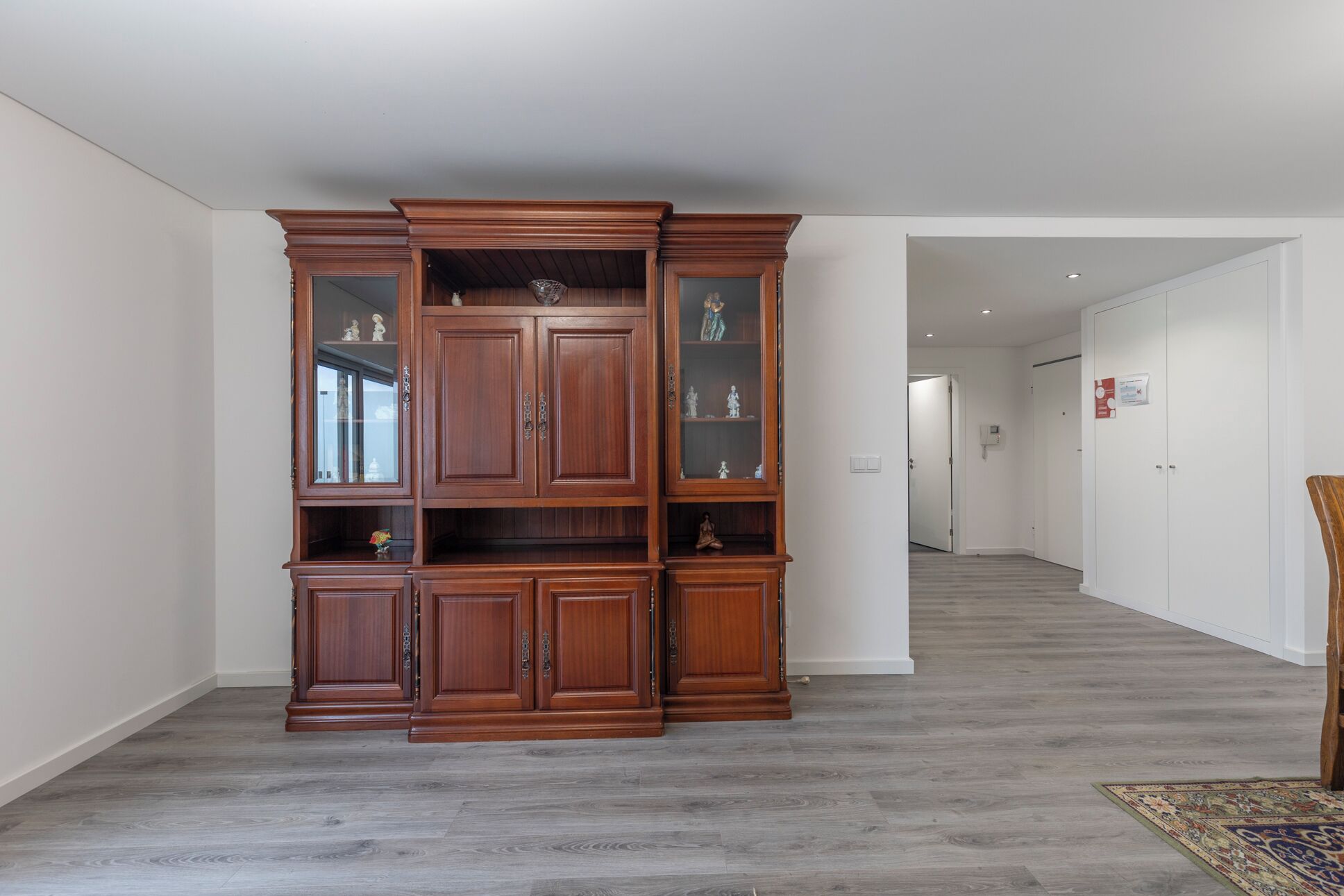 A spacious room with a large wooden cabinet, a patterned rug, and a door leading to another area.