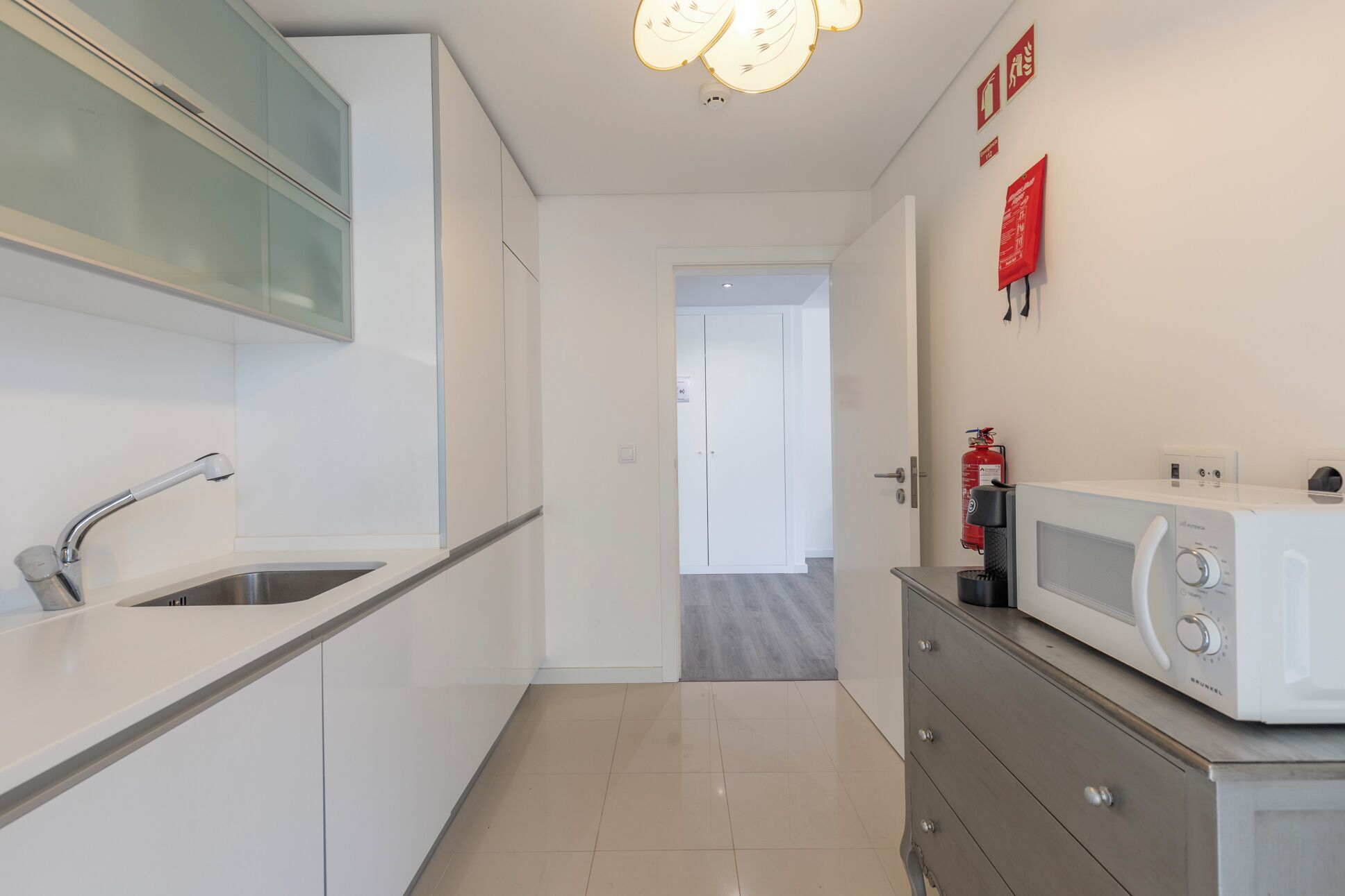 A modern kitchen with a stainless steel sink, a microwave, and a fire extinguisher on the wall.