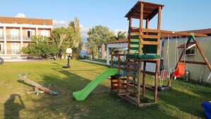 A playground with a slide, swings, and a climbing structure. - Olive Trees Garden Lixouri (Kefalonia)