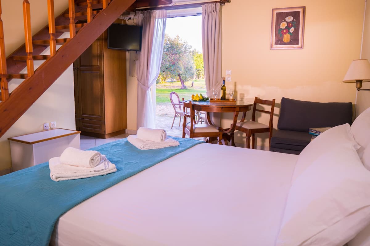 Habitación de hotel con cama, escritorio, silla, mesa con una botella y vasos, y una escalera.
