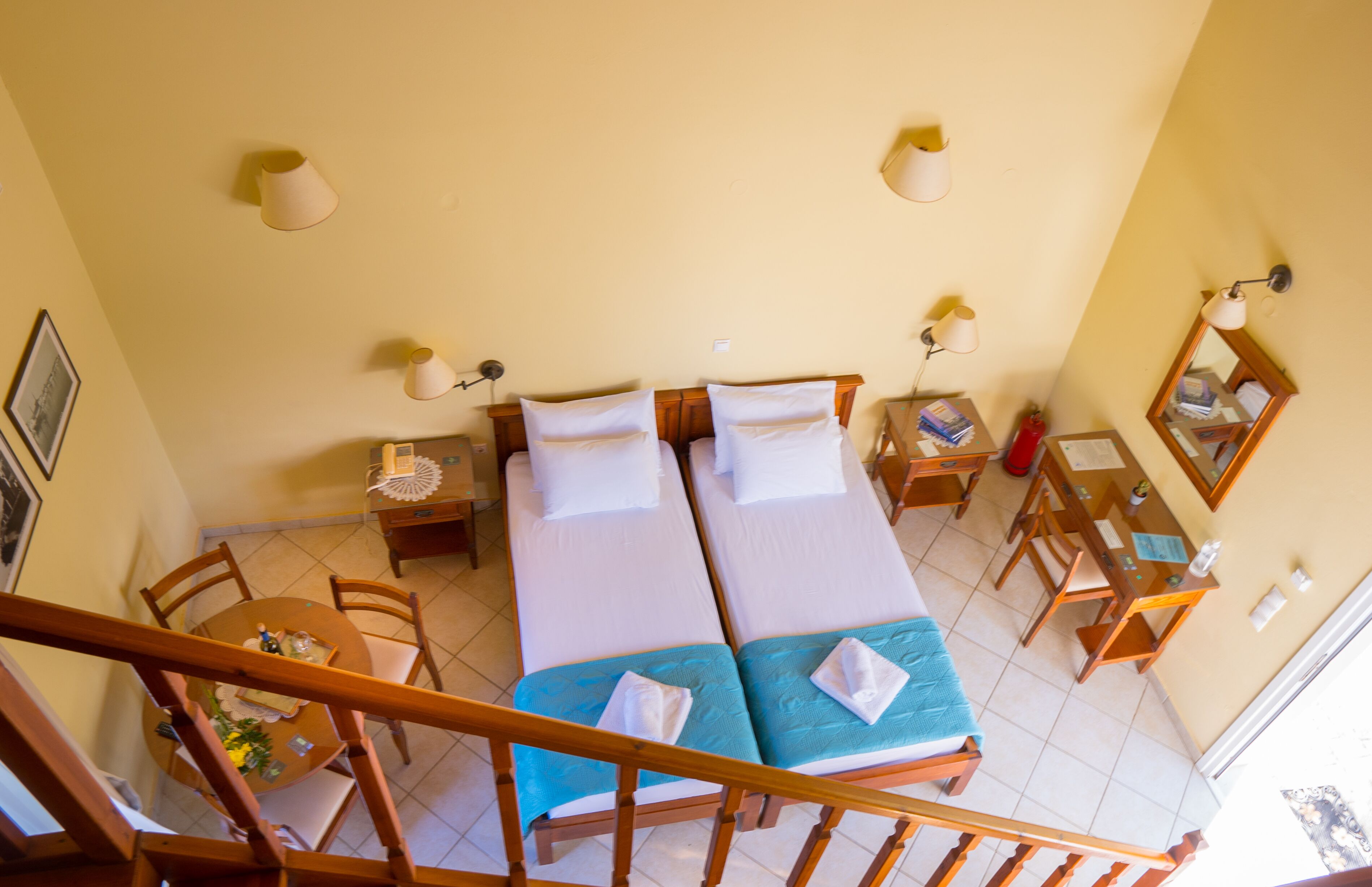 A hotel room with two beds, a desk, chairs, a dining table, and a staircase.