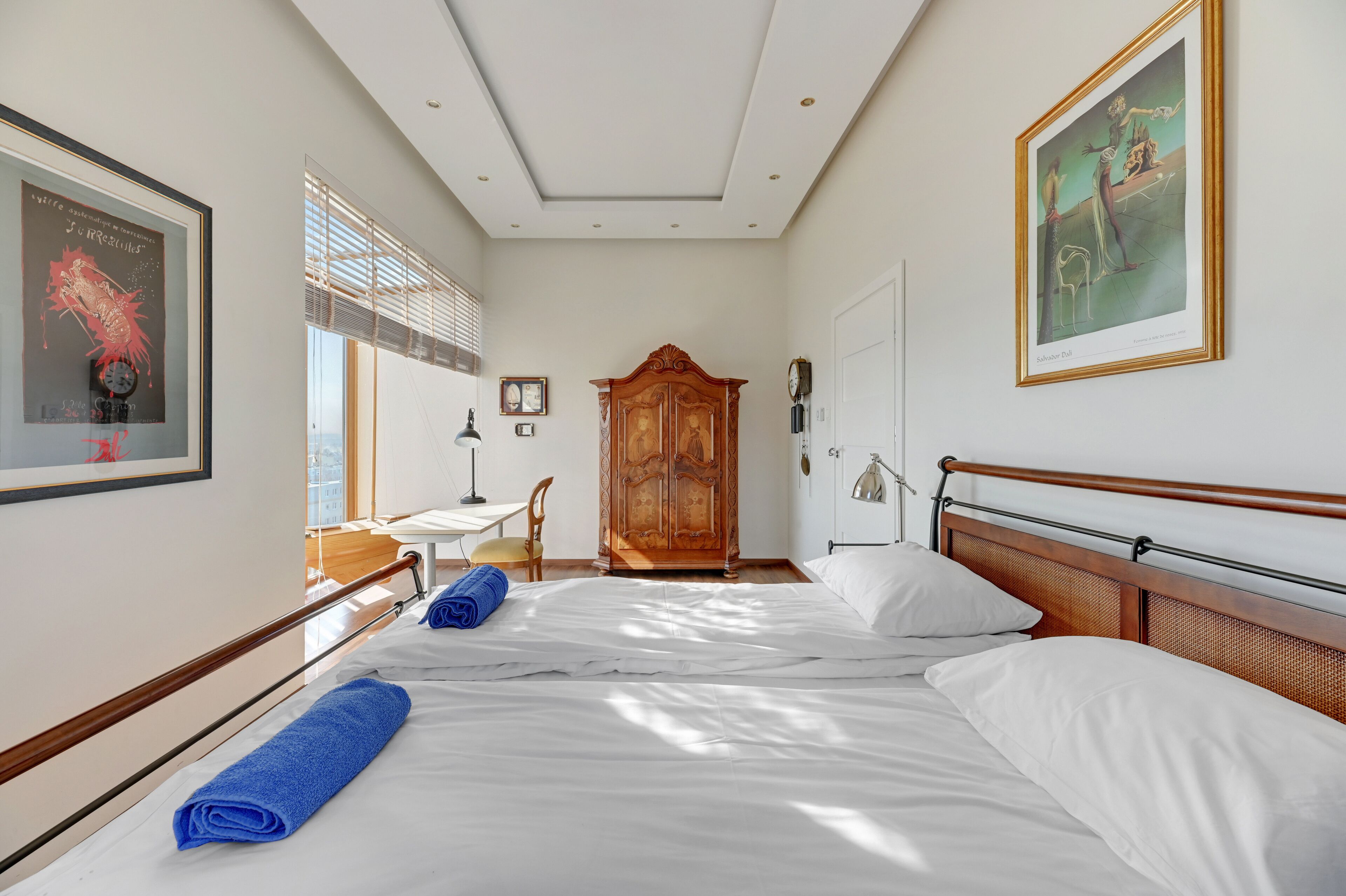 A hotel room with a large bed, a wooden wardrobe, a desk, and a chair.
