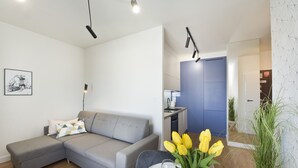 Ein modernes Wohnzimmer mit einer grauen Eckcouch, einem Esstisch für zwei Personen und einer Küche im Hintergrund.
