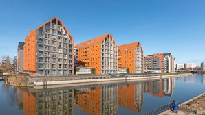 Ein modernes Gebäude mit einem spiegelnden Wassenspiegel davor, ausgestattet mit mehreren Balkonen und großen Fenstern.