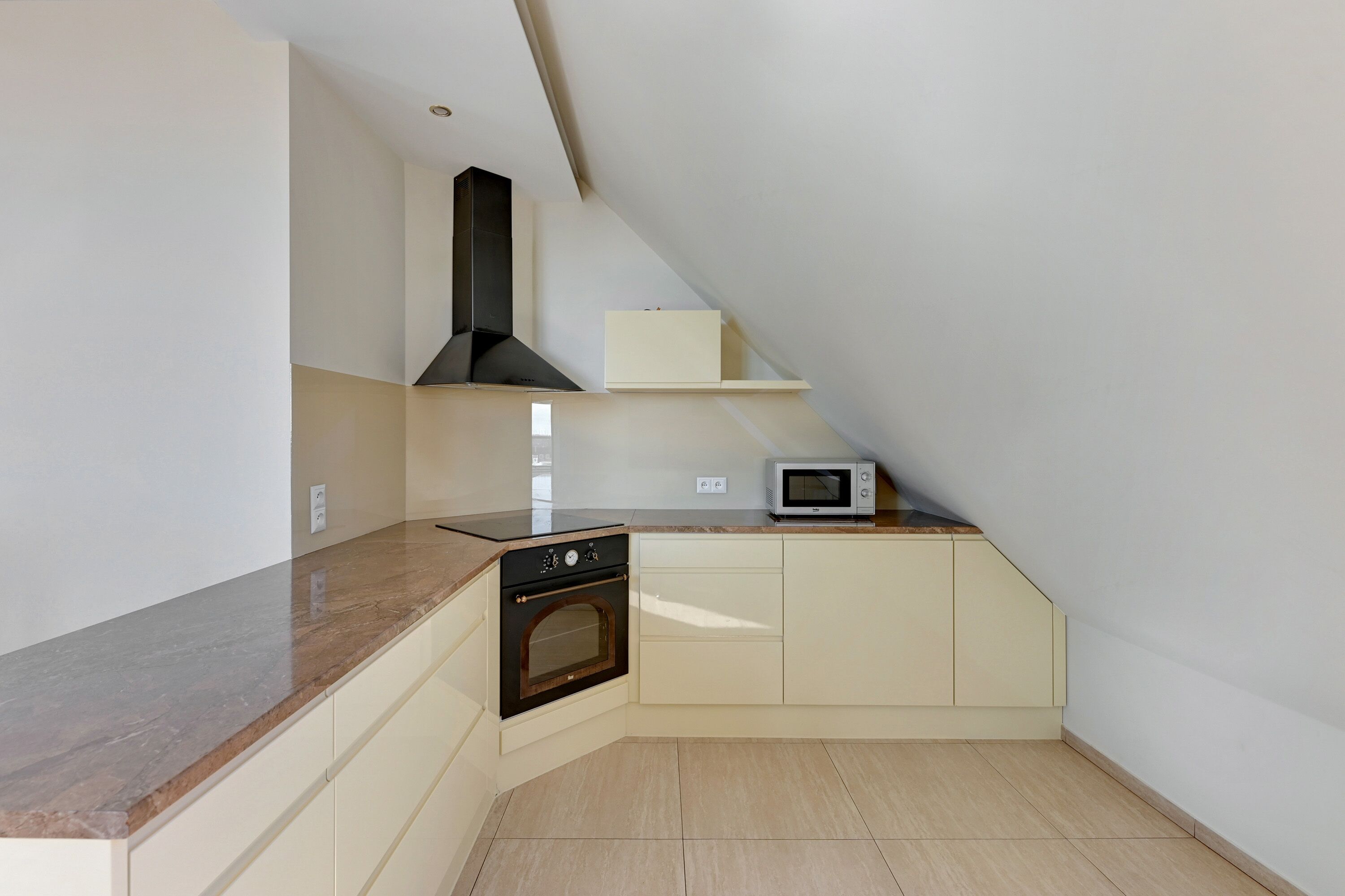 Cocina compacta con horno empotrado, microondas y extractor de aire negro.