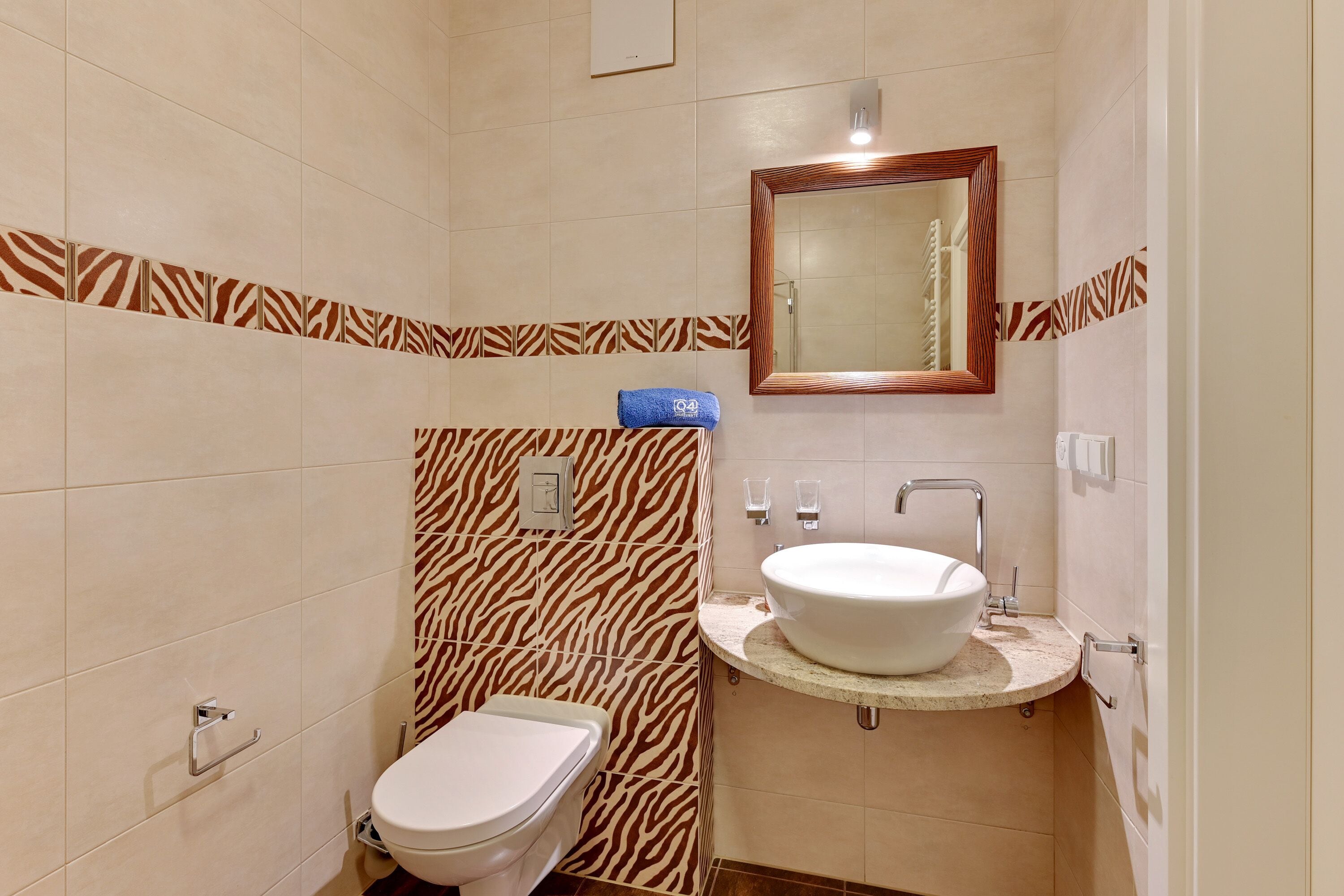 Een badkamer met een muur in zebraprint, een wit toilet, een wastafel met spiegel erboven en een handdoek aan de muur.
