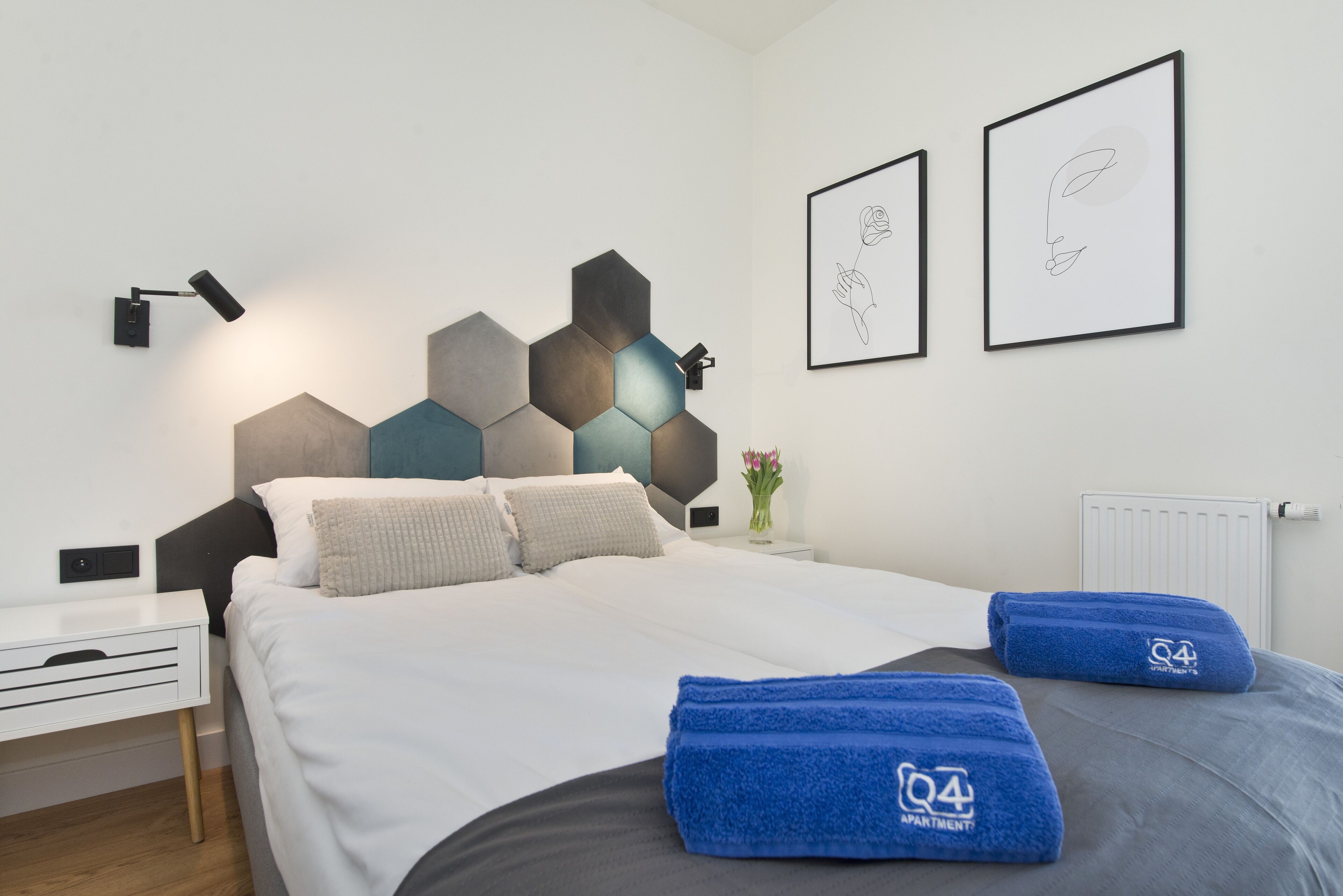 Ett modernt hotellrum med en snyggt bäddad säng, ett sängbord och en väggmonterad lampa.