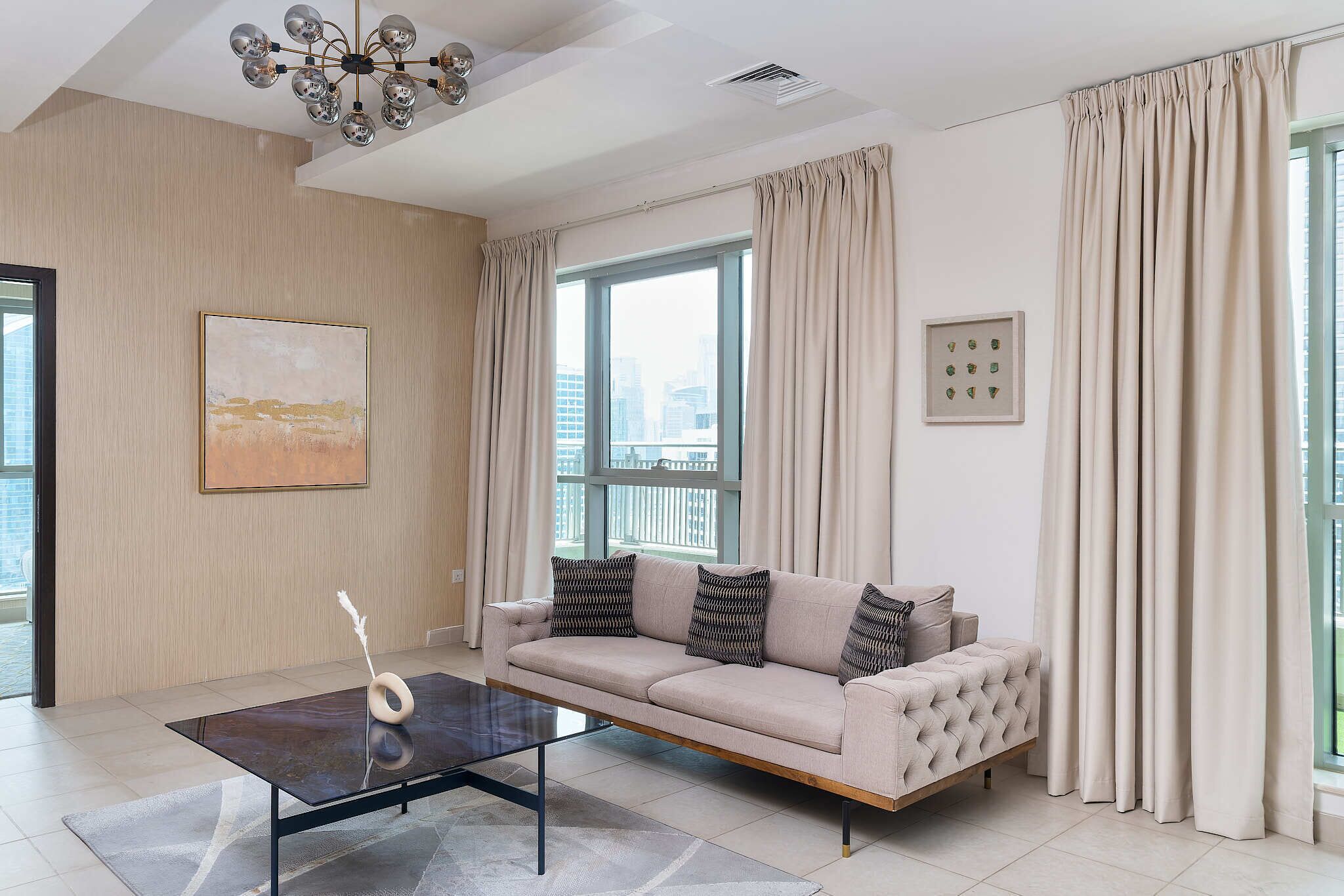 A modern living room with a sofa, a coffee table, and a city view through large windows.