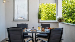 Ruokapöytä tuoleineen, kannu, kuppi ja lautanen täynnä ruokaa.