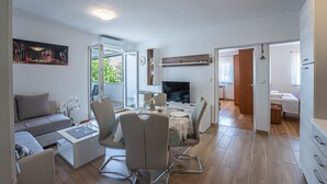 Moderni olohuone, jossa on sohva, sohvapöytä ja televisio. Siellä on myös ruokailutila, jossa on tuoleja ja pöytä, sekä makuuhuone, jossa on sänky ja ikkuna.