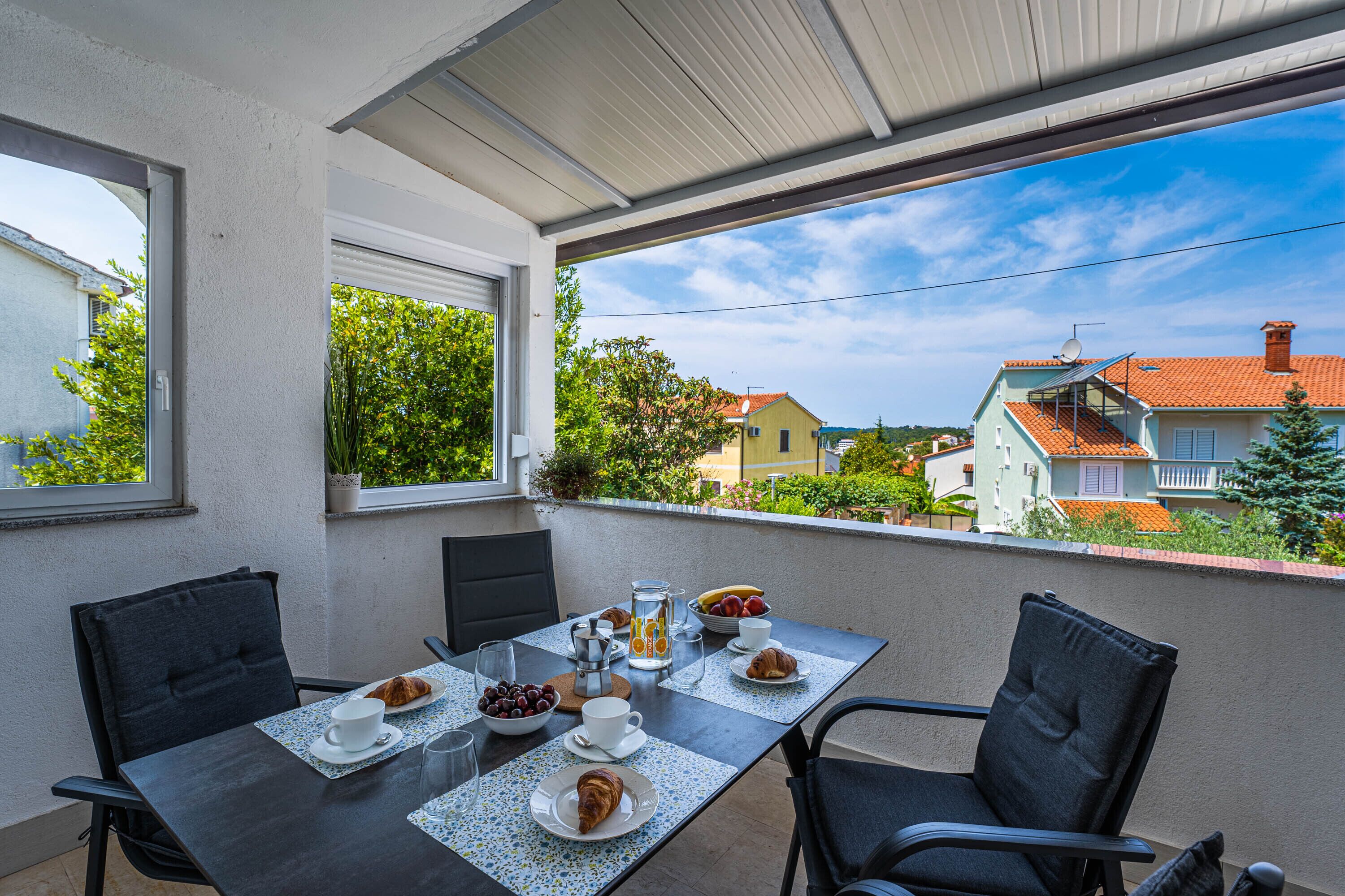 Un balcón con una mesa lista para el desayuno, sillas y vistas al vecindario.