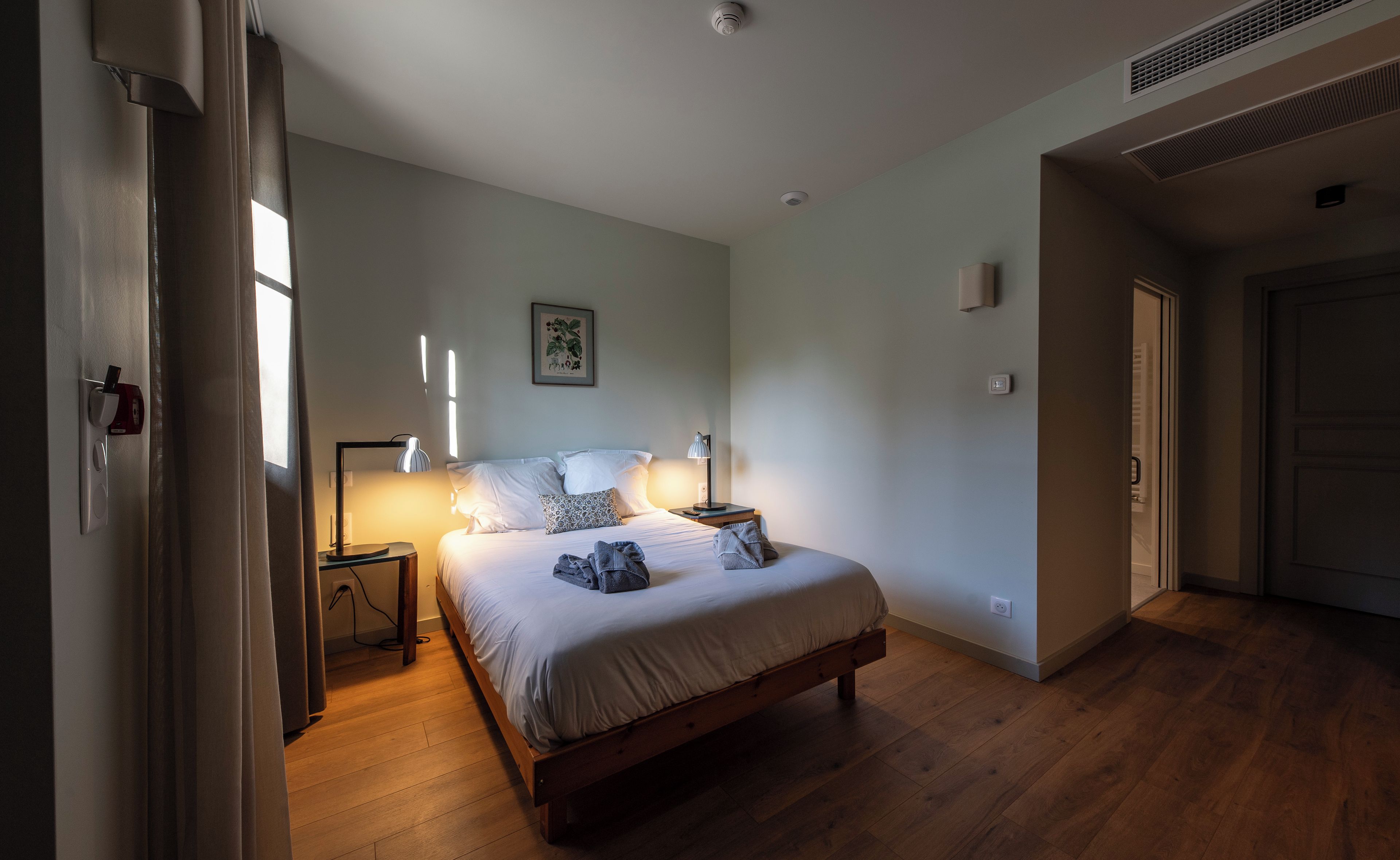 Un dormitorio con cama de madera, lámparas de noche, un cuadro en la pared y una puerta a otra habitación.