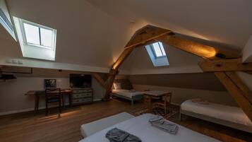 Une chambre située dans un espace de type « loft », avec un plafond en pente, deux lits, un bureau et un téléviseur.