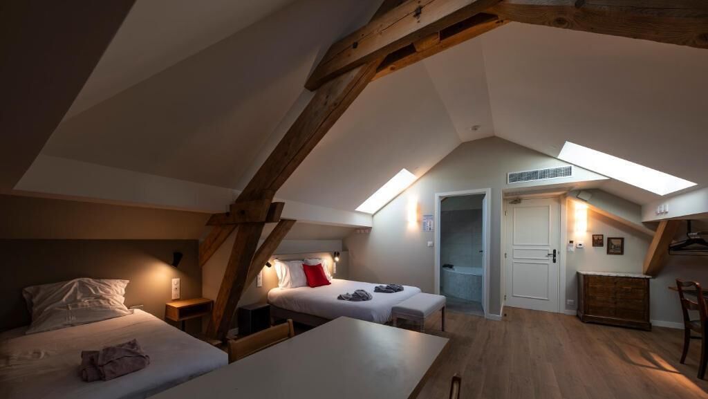 Et hyggeligt soveværelse på loftet med skråvægge, ovenlysvindue, seng, lille bord og stol.