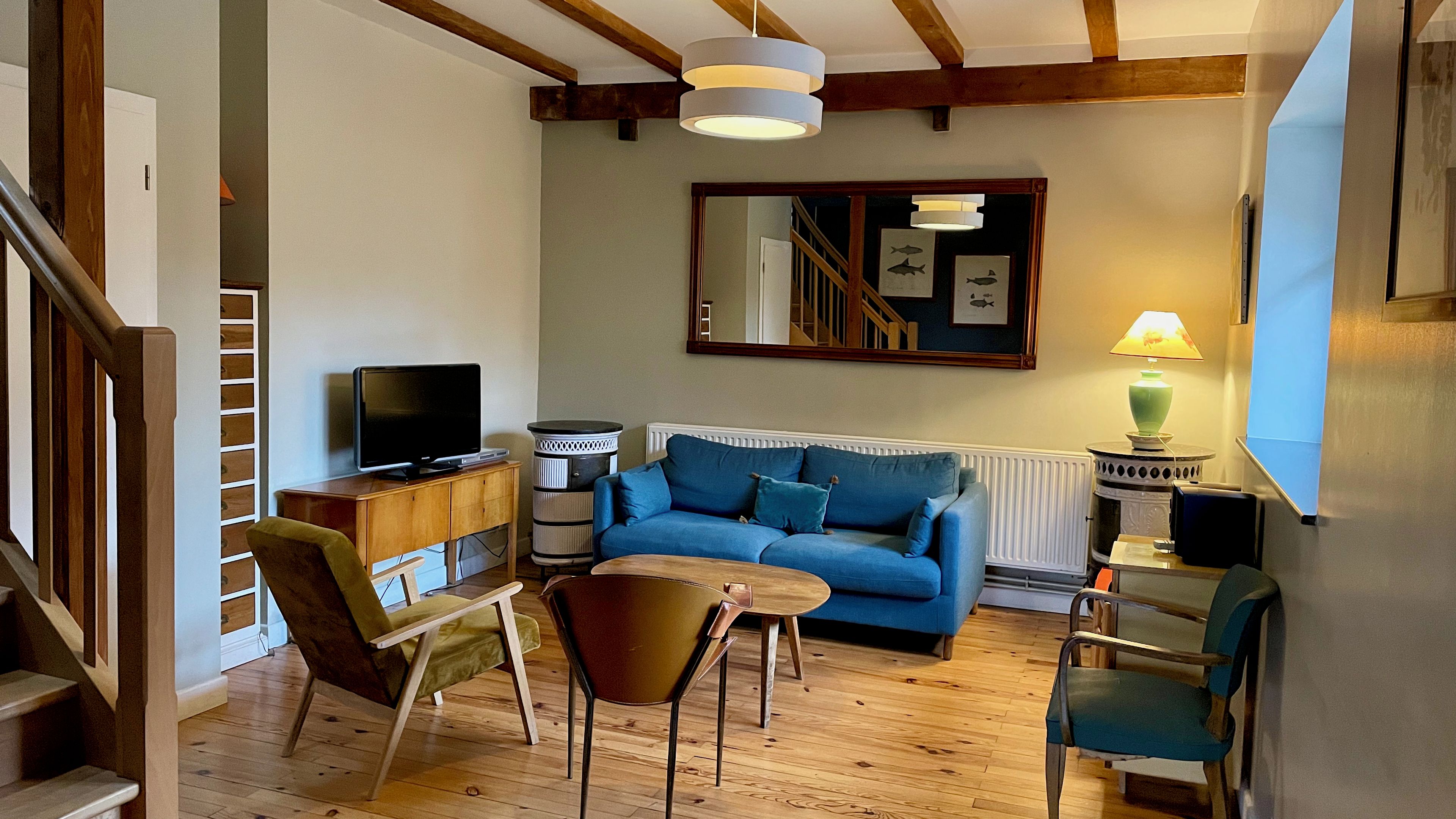 Un salón acogedor con un sofá azul, suelo de madera y un televisor sobre un mueble de madera.