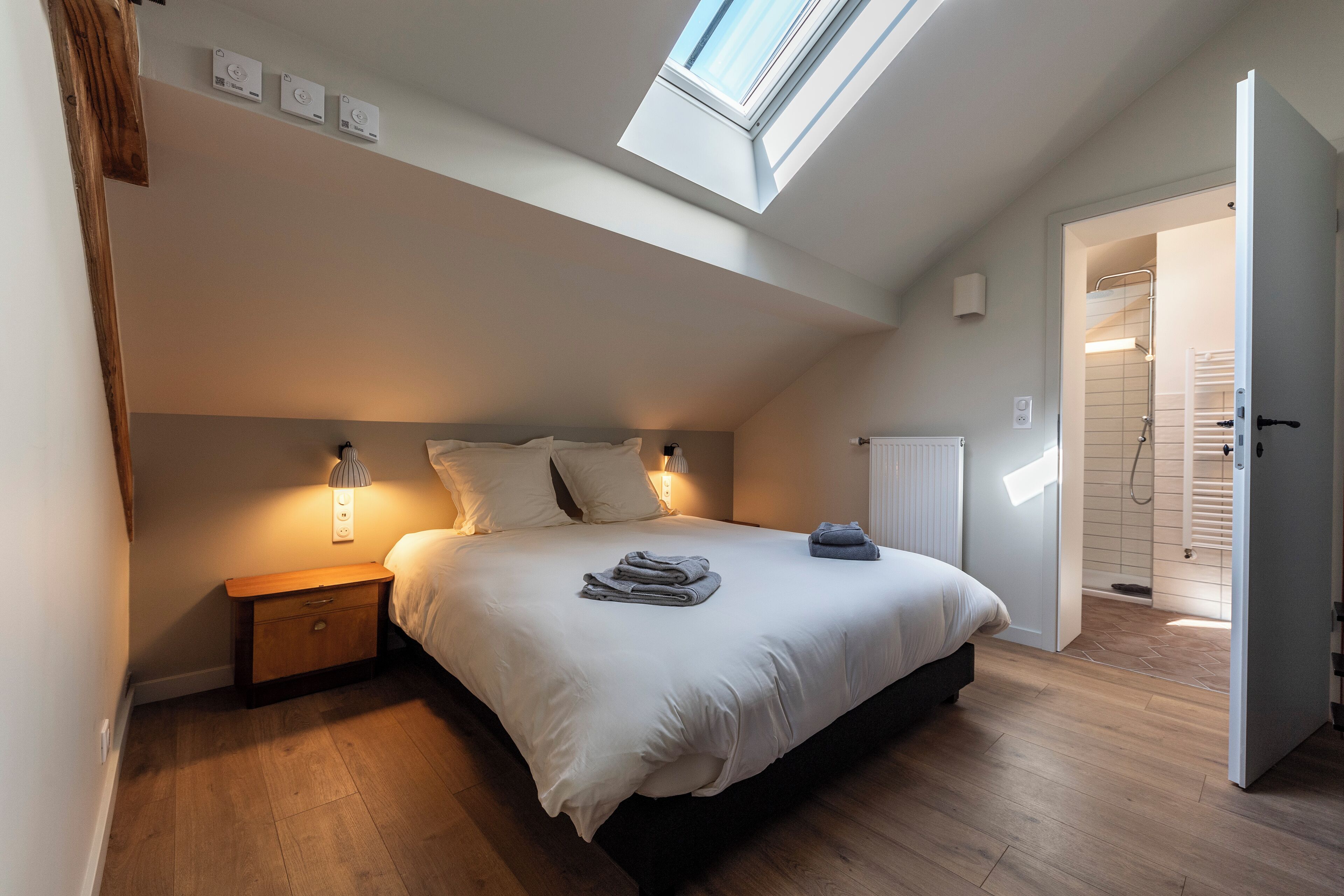 A bedroom with a skylight, a bed with pillows, a nightstand, and a bedside table.