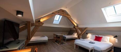 Un dormitorio estilo loft con techo inclinado, una cama, un escritorio y un televisor.