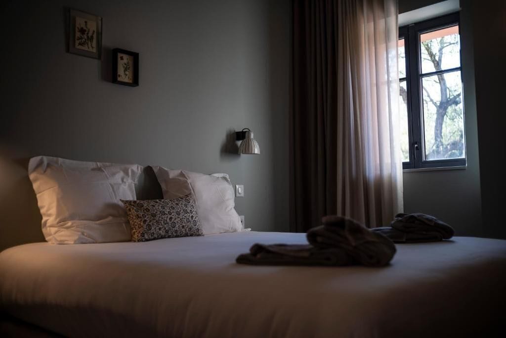 A bedroom with a bed, pillows, a lamp, and a window with curtains.