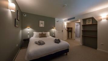 A bedroom with a bed, bedside tables, a wardrobe, and a door leading to another room.