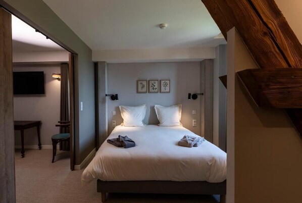 A bedroom with a bed, bedside lamps, a flat-screen TV, and a small table with a chair.