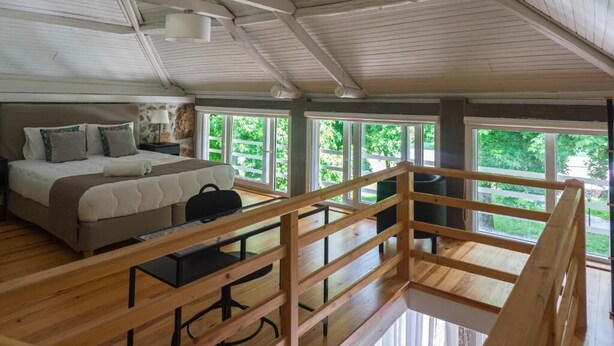 A bedroom with a bed, bedside table, and a view of greenery through large windows. - Casas do Souto (Lousada)