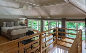 A bedroom with a bed, bedside table, and a view of greenery through large windows. - Casas do Souto (Lousada)