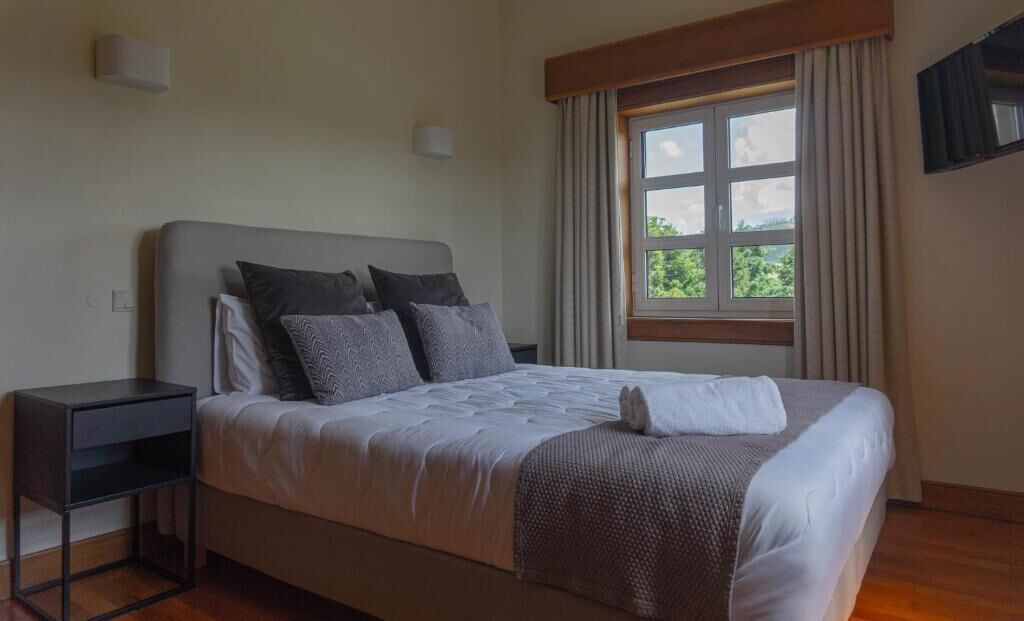 A neatly made bed with a white and brown blanket, a bedside table, and a window with curtains.