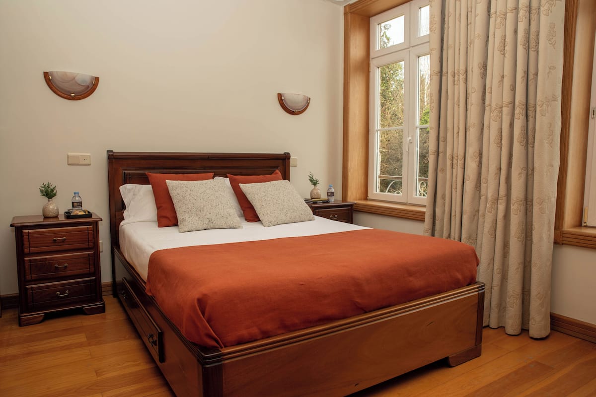 A neatly arranged bedroom with a wooden bed, two bedside tables, a nightstand, and a window with curtains.