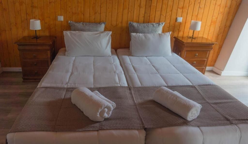 A double bed with two pillows and a blanket, wooden headboard, nightstands with lamps, and a wooden floor.