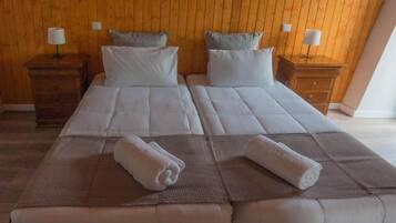 A double bed with two pillows and a blanket, wooden headboard, nightstands with lamps, and a wooden floor.