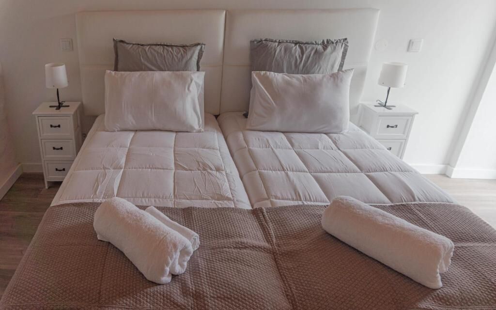 Una cama doble con dos almohadas, una mesita de noche con lámpara y una toalla doblada sobre la cama.