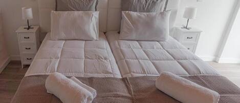 Una cama doble con dos almohadas, una mesita de noche con lámpara y una toalla doblada sobre la cama.