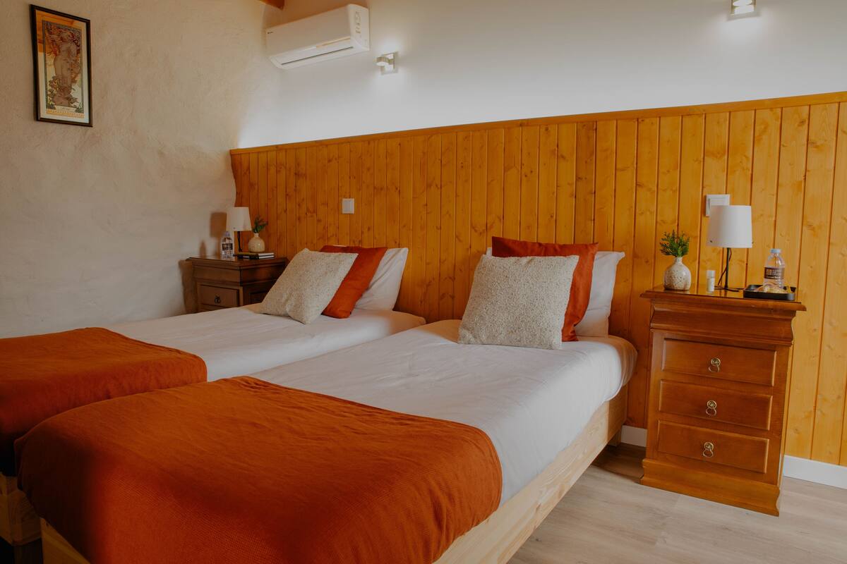 A room with two beds, wooden headboard, bedside tables with lamps, and a small dresser.