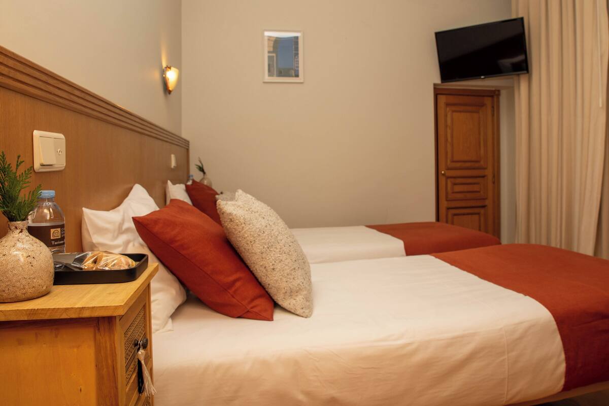 A hotel room with two beds, a TV, a small window, and a wooden cabinet.