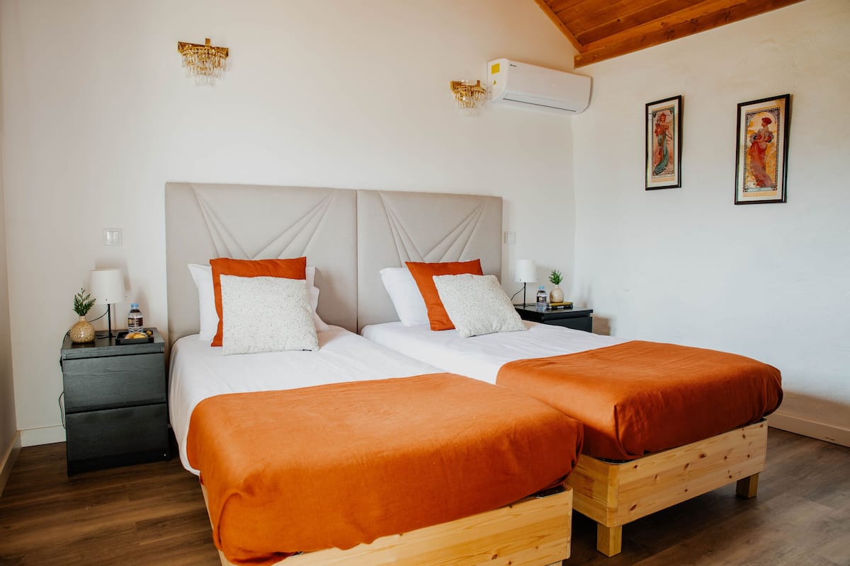 A double bed with two single beds, a wooden headboard, a nightstand with a lamp, and a wall-mounted air conditioner.