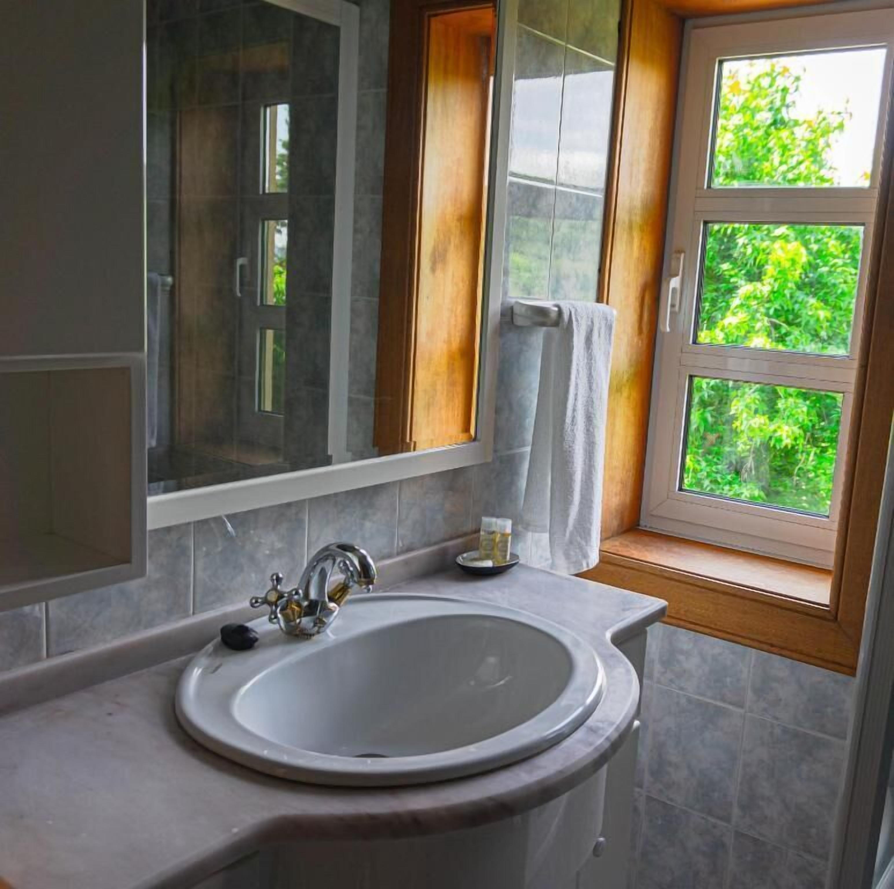 Un bany amb un gran mirall, un lavabo i una finestra que dona a zones verdes.