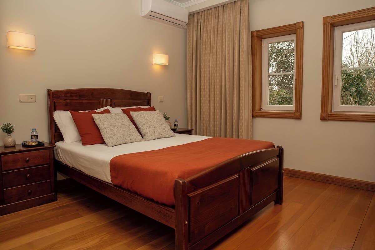 A neatly made bed with a wooden headboard, two bedside tables, and a window with curtains.
