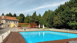 A swimming pool with a wooden deck, surrounded by trees and a building with a red roof. - Casas do Souto (Lousada)