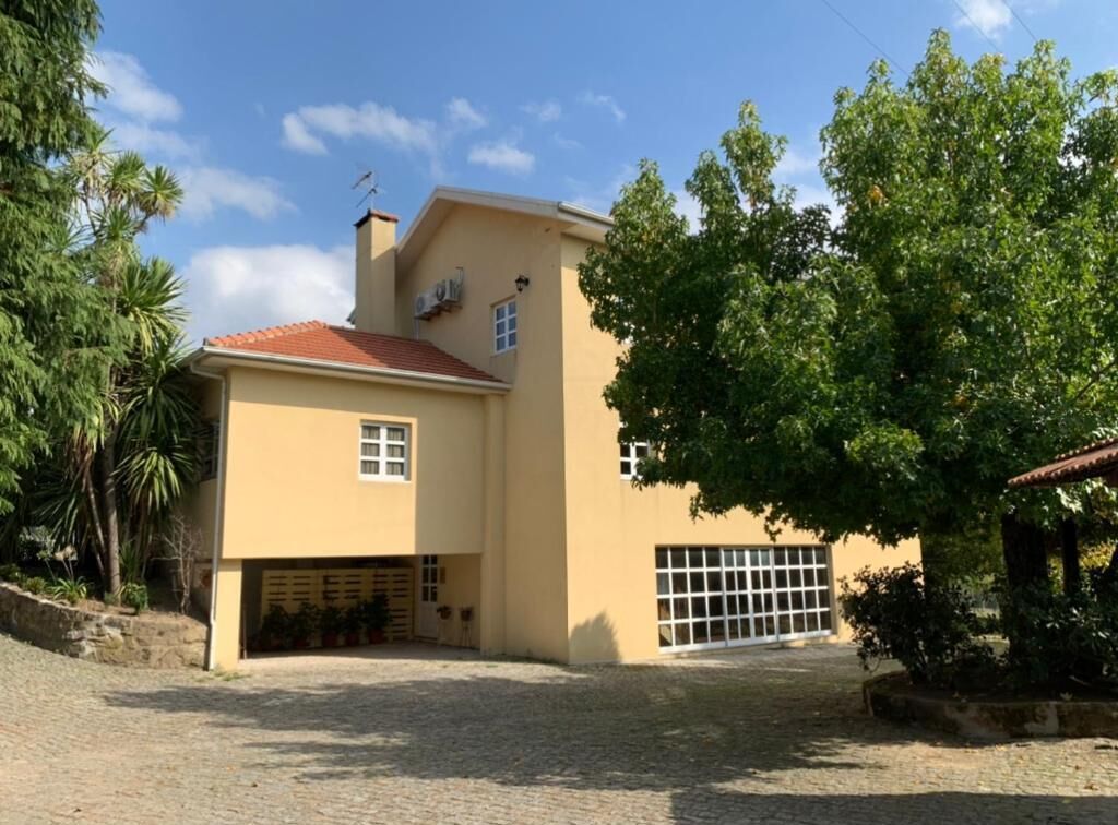 A two-story house with a garage, a covered driveway, and a small garden area with trees and shrubs.