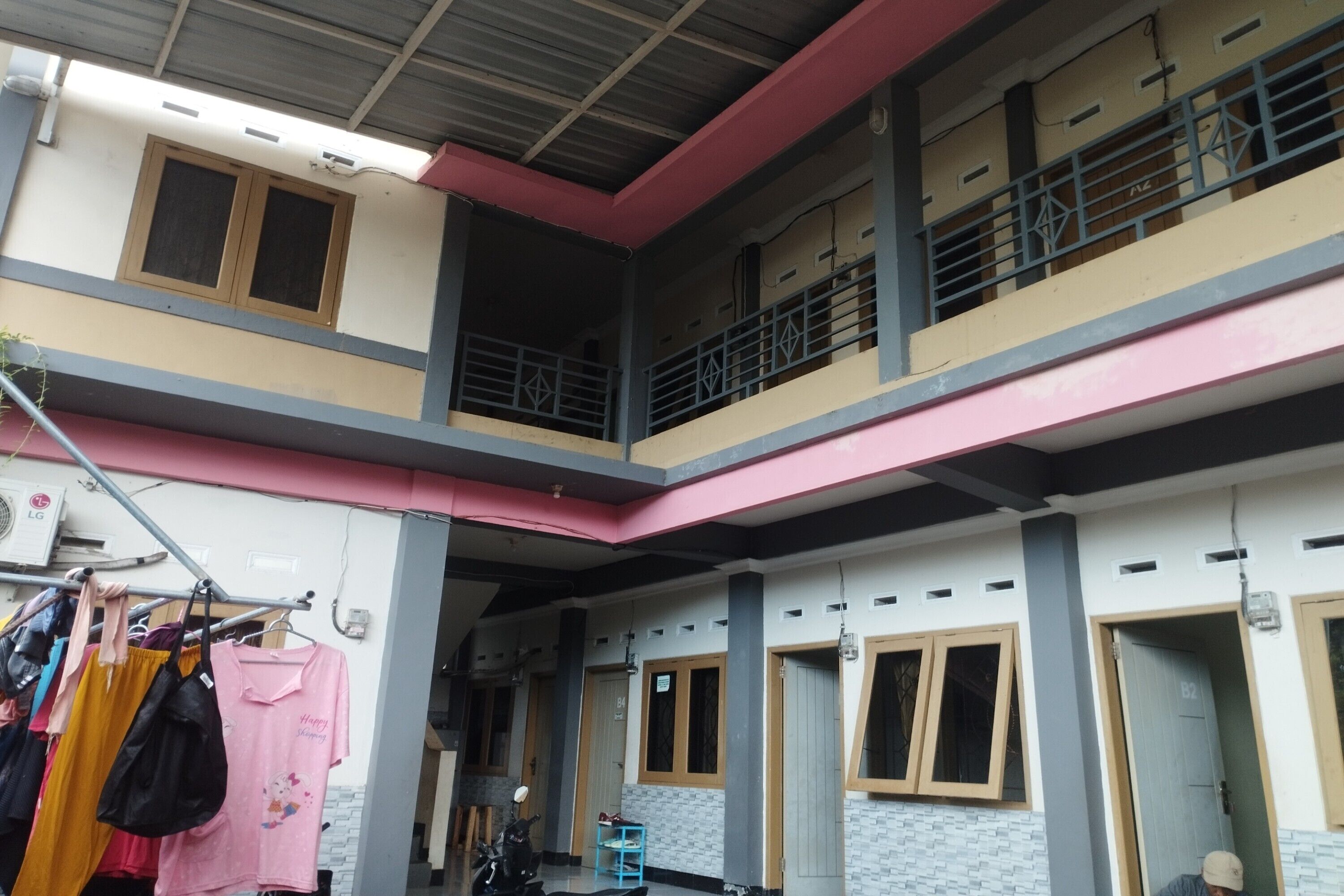 A multi-level building with a balcony on the upper floor, a clothing rack with various garments, and a motorcycle parked inside.