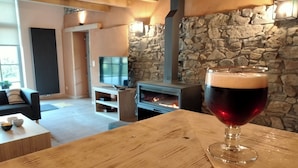 A cozy living room with a stone wall, a fireplace, and a glass of beer on a wooden table.