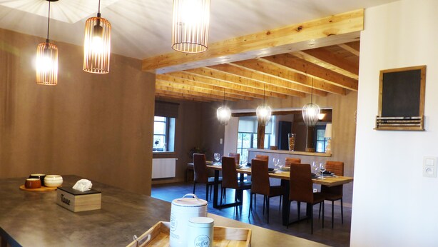 A modern kitchen with wooden beams, pendant lighting, and a dining area with chairs and a table.
