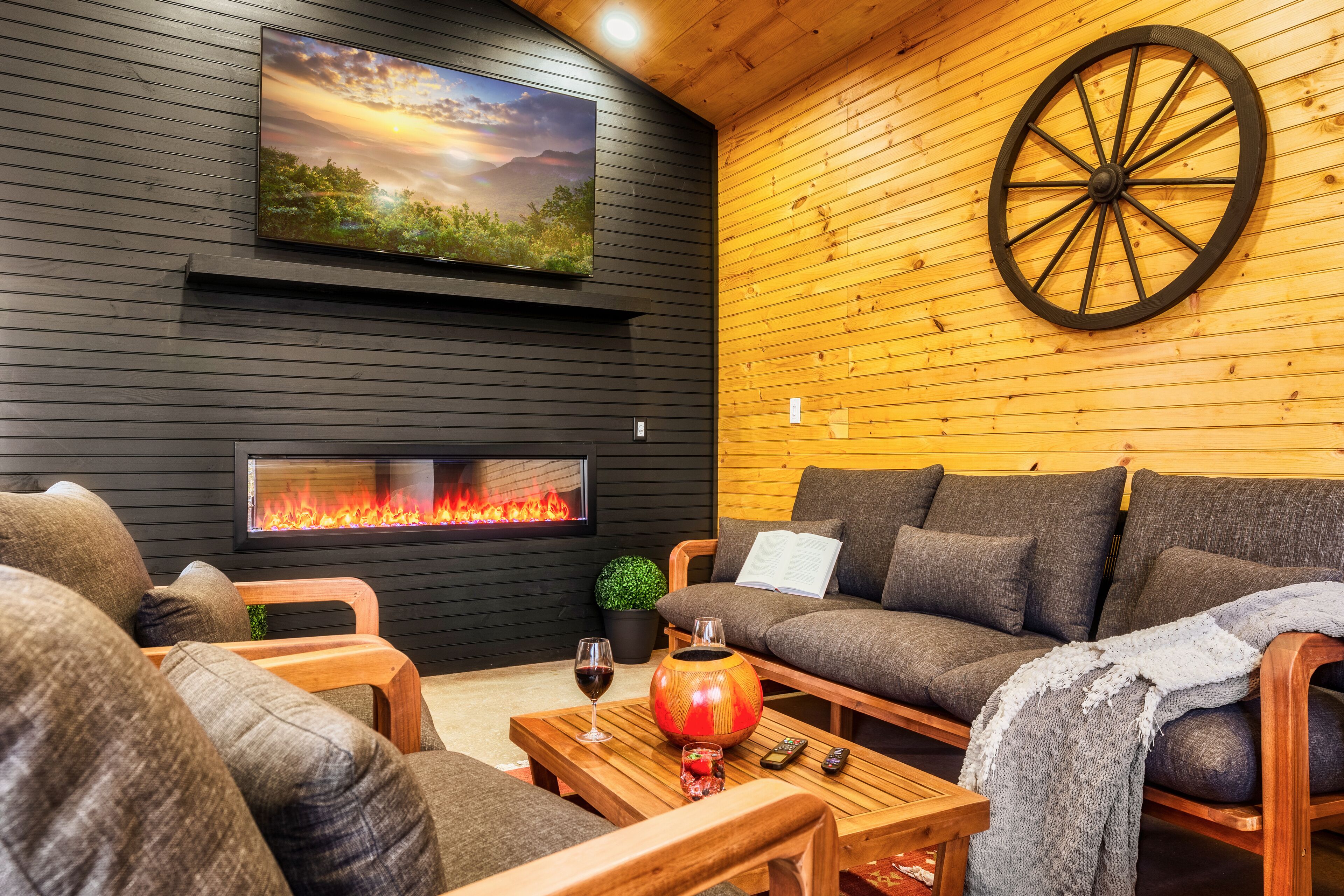 A cozy living room with a fireplace, a large wooden wheel, and a flat-screen TV mounted on the wall.