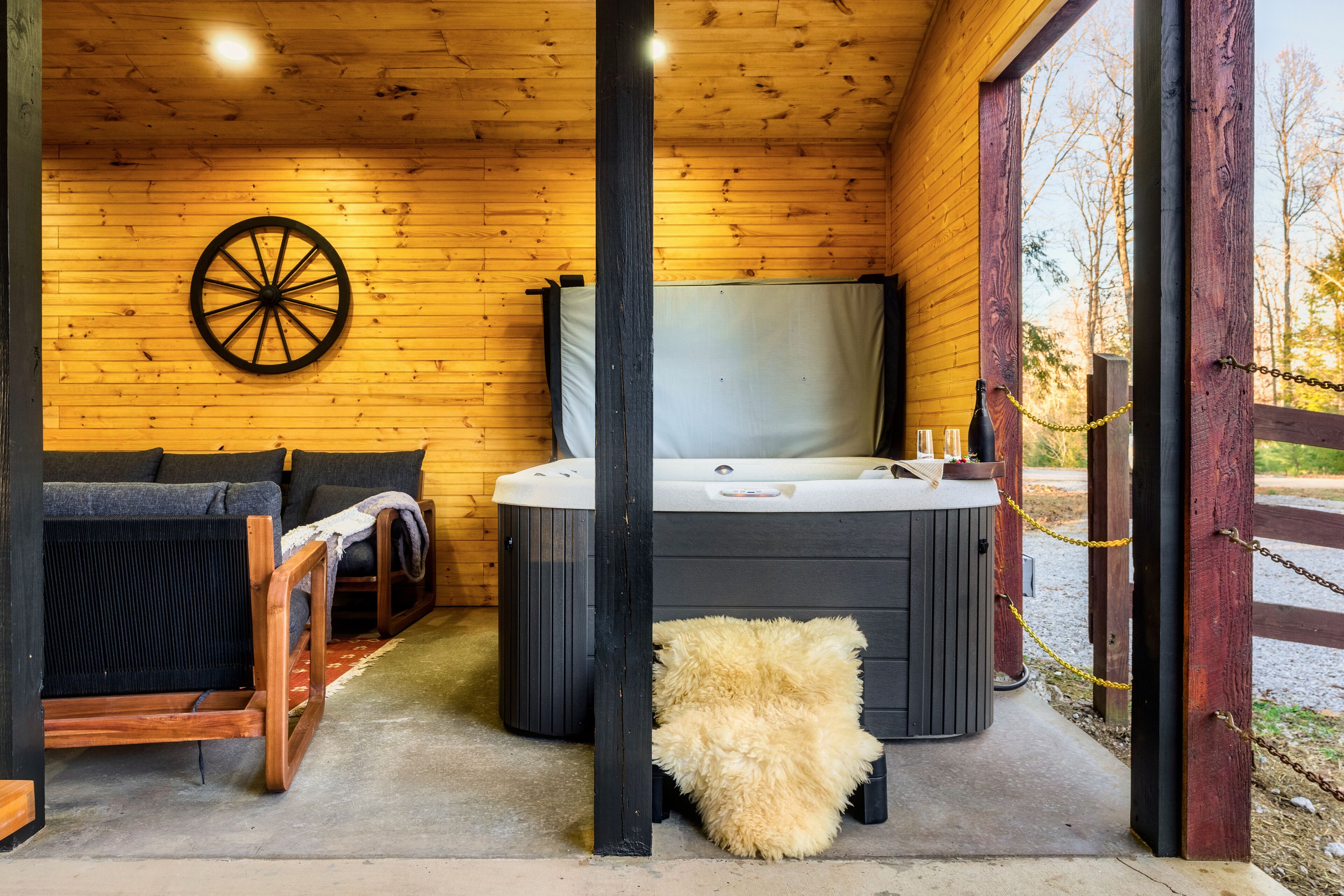 A wooden cabin interior with a hot tub, a sofa, and a large wheel on the wall.