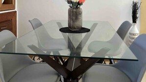 A modern dining area with a glass table, grey chairs, a decorative mirror, and a vase with flowers. - TiniTara Cozy Home (Dar es Salaam, Tanzania)
